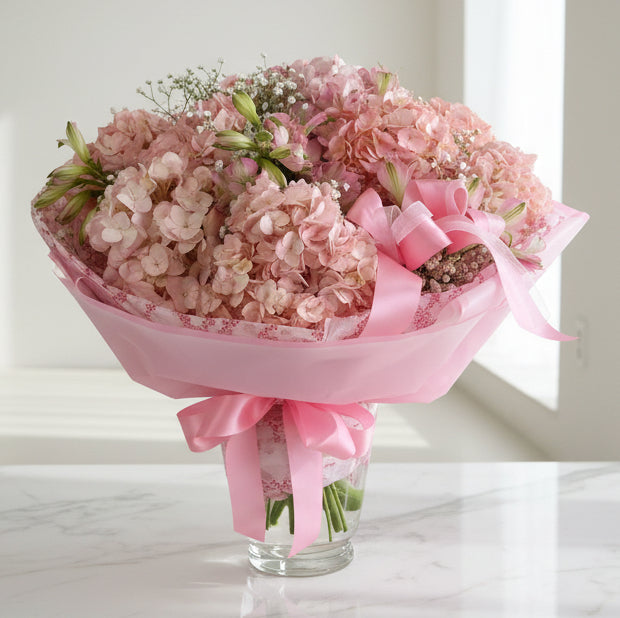 Bouquet of pink flowers in a glass vase with pink ribbon on a white surface.